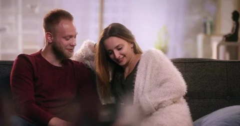 Young couple sitting on sofa and looking at tablet Stock Footage 77397918