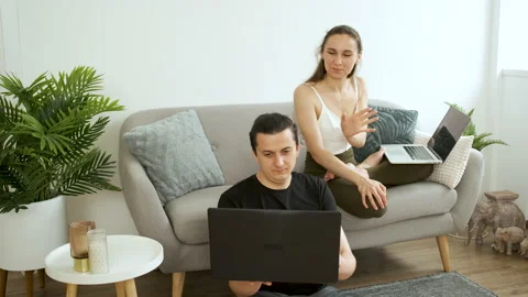 Young couple sitting on sofa and floor meditating and working on laptop. Work at Stock Footage 140755822