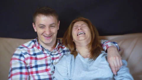 Young couple is sitting on the sofa, laughing and watching TV. Video stock 100870042