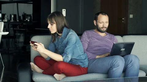 Young couple sitting on sofa, man with laptop, woman playing game Stock Footage 63218022