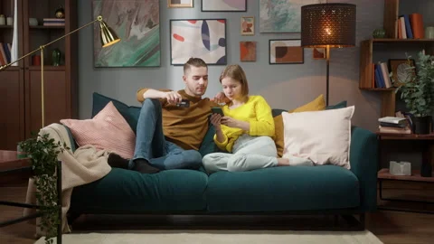 Young Couple sitting on sofa staying at home using smartphone for online Video stock 153092895