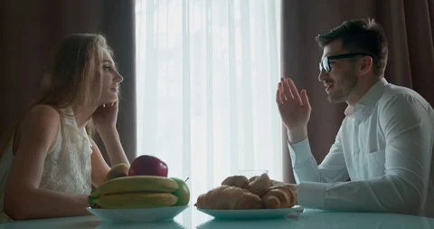 Young couple sitting at the table and talking. On the table are fruits and Stock Footage 121796387