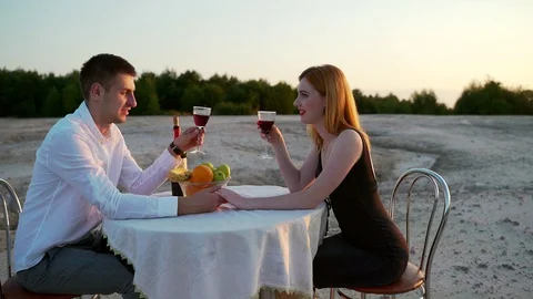 Young couple sitting at a table in nature. first romantic date on the sandy  Stock Footage 128459908