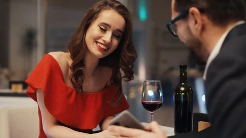 Young couple sitting at table in restaurant and looking at own smartphones. Girl Stock Footage 88096416