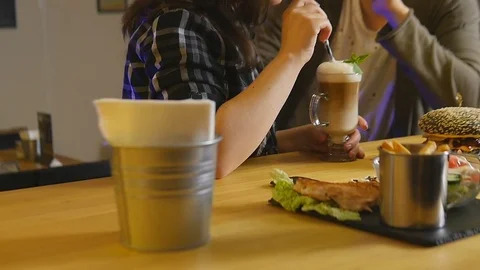 Young couple sitting at a table on which are burgers coffee and salad Stock Footage 76158231