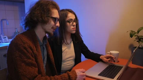 Young couple sitting together on kitchen using laptop, internet shopping or Stock Footage 242993369