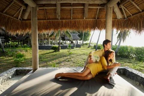 Young couple sitting under thatch cabana Stock Photos