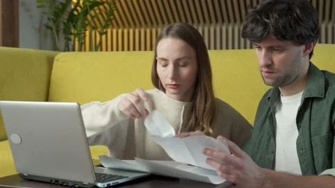 Young couple sitting on yellow sofa at home and managing budget using laptop Stock-Footage 148120384