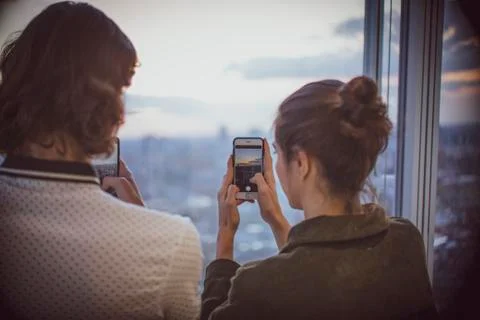 Young couple with smart phones photographing sunset at highrise window Stock Photos