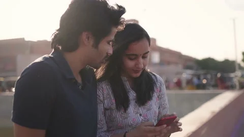 A young couple is smiling and talking outdoors while using a mobile phone Stock Footage 151959009