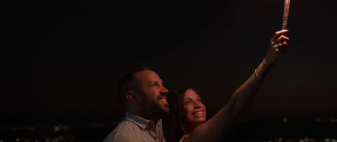 Young couple smiling while holding a firework on the hill at night Stock Footage 136239836