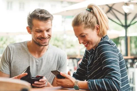 Young couple smiling while looking at their phone, sitting at a bar waiting for Stock Photos