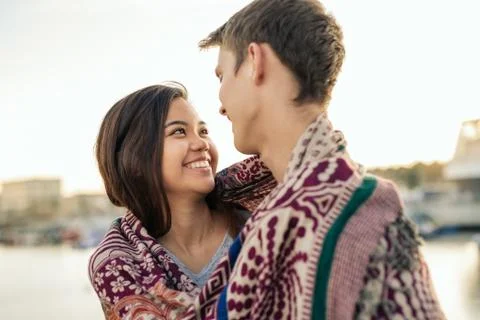 Young couple smiling while wrapped in a blanket together outside Stock Photos