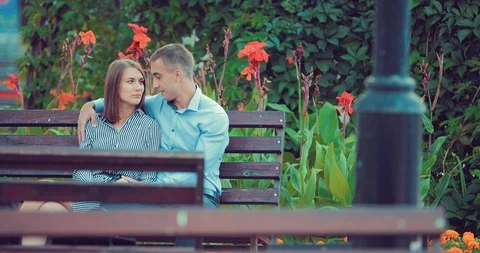 Young couple spend time together on a bench in a holiday park Stock Footage 94137410