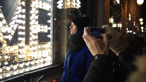 Young couple spends time together on busy city street in evening taking photo Stock Footage 83874431