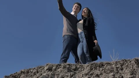 Young couple stand on a hill, in the background a blue sky, sunny spring day Stock Footage 124425722