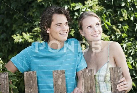 Young couple standing behind wood fencing, smiling Stock Photos