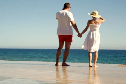 A young couple standing hand in hand on the beach, slow motion Stock Footage 1068476