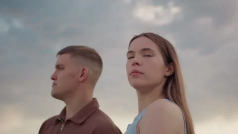Young couple standing under cloudy sky with thoughtful expressions Video stock 317147939