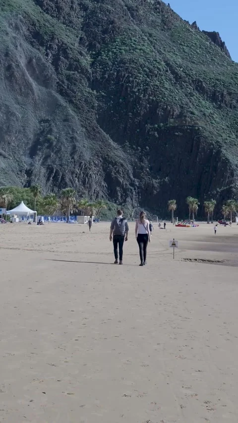Young couple strolling on a sandy beach below a scenic mountain Video stock 329866286