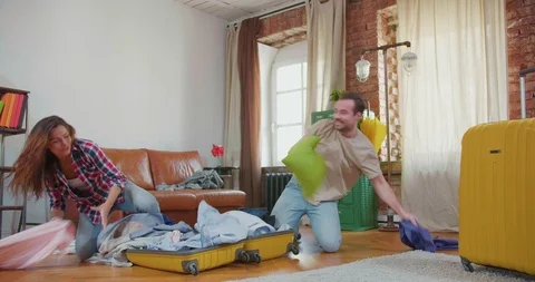 Young couple stuff things into suitcase in mess. Stock Footage 107933137