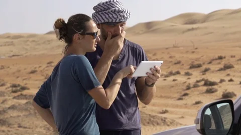 Young couple with tablet checking map standing near car on dessert Video stock 78879218