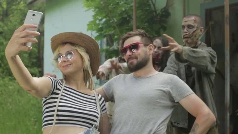 A young couple takes a selfie on the background of linked zombies. Vídeo Stock 77476431
