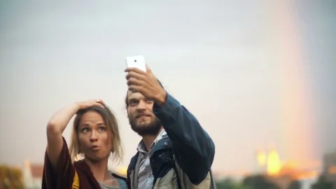 Young couple taking selfie photos with rainbow on background. Cheerful man and Stock Footage