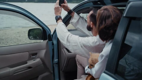 Young couple taking a selfie with their dog in a car near the beach Stock Footage 328558368