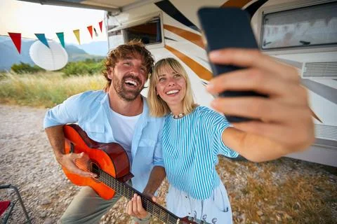 A young couple is taking a selfie while playing guitar at the campsite in t.. Stock Photos