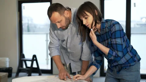 Young couple talking and checking blueprints at their new home Stock Footage 63994200