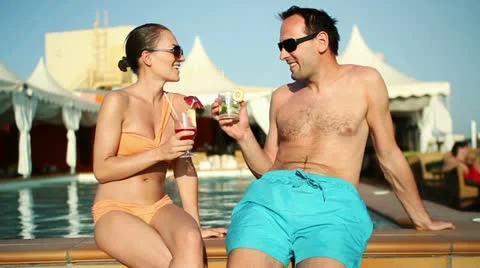 Young couple talking and drinking exotic cocktails by the pool HD Stock Footage 10862514