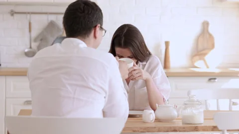 Young couple talking and drinking coffee while sitting at table in home kitchen Stock Footage 162726828