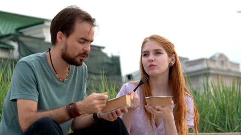 Young couple talking and eating takeaway food while sitting on stairs in street Stock Footage 177359698