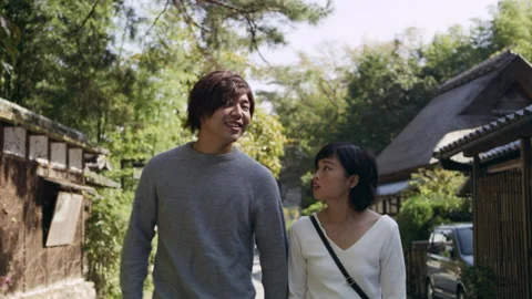 Young couple talking and walking past houses down a sidewalk in Kyoto, Japan wit Video stock 199461511