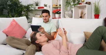 Young Couple Talking Browsing a Digital Tablet Positive Activity Sitting on Sofa Stock Footage 85542007