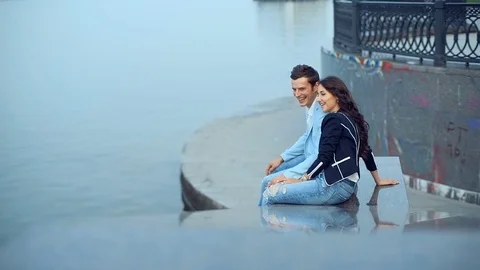 Young couple talking with smile while sitting near the river at the embankment Stock Footage 71796997