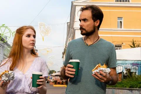 Young couple talking while walking along city street and eating takeaway food Stock Photos