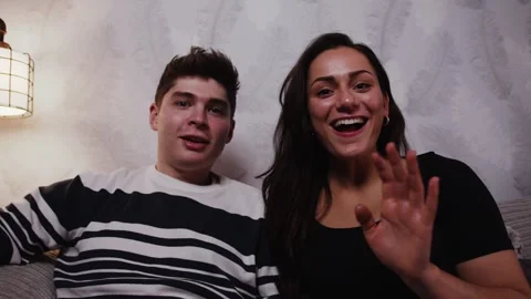 Young couple taps on a touchscreen device and waves hello Stockbeeldmateriaal 242999594