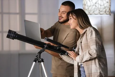 Young couple with telescope using laptop in room at night Fotos Stock