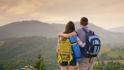 Young couple of travelers looking forward to the horizon and mountains, rear Stock Footage