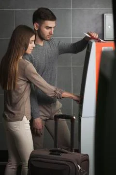 Young couple using ATM machine at airport Stock Photos