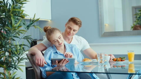 Young couple using digital tablet while having breakfast at kitchen table Видео 86719528