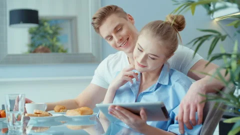 Young couple using digital tablet while having breakfast at kitchen table. Stock Footage 86719727