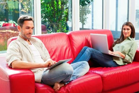 Young couple using digital tablet and laptop on sofa Stock Photos