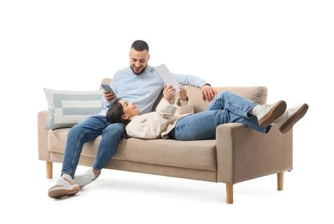 Young couple using gadgets on grey sofa against white background Stock Photos