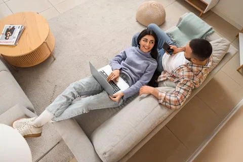 Young couple using gadgets on grey sofa at home, top view Stock Photos