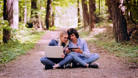 Young Couple Using Laptop And Tablet While Sitting In Forest Video stock 89892292