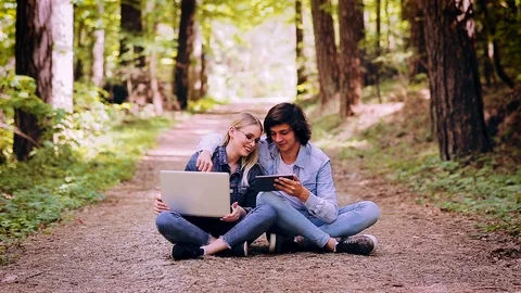 Young Couple Using Laptop And Tablet While Sitting In Forest Video stock 89892379