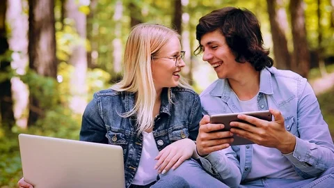 Young Couple Using Laptop And Tablet While Sitting In Forest Video stock 89893369